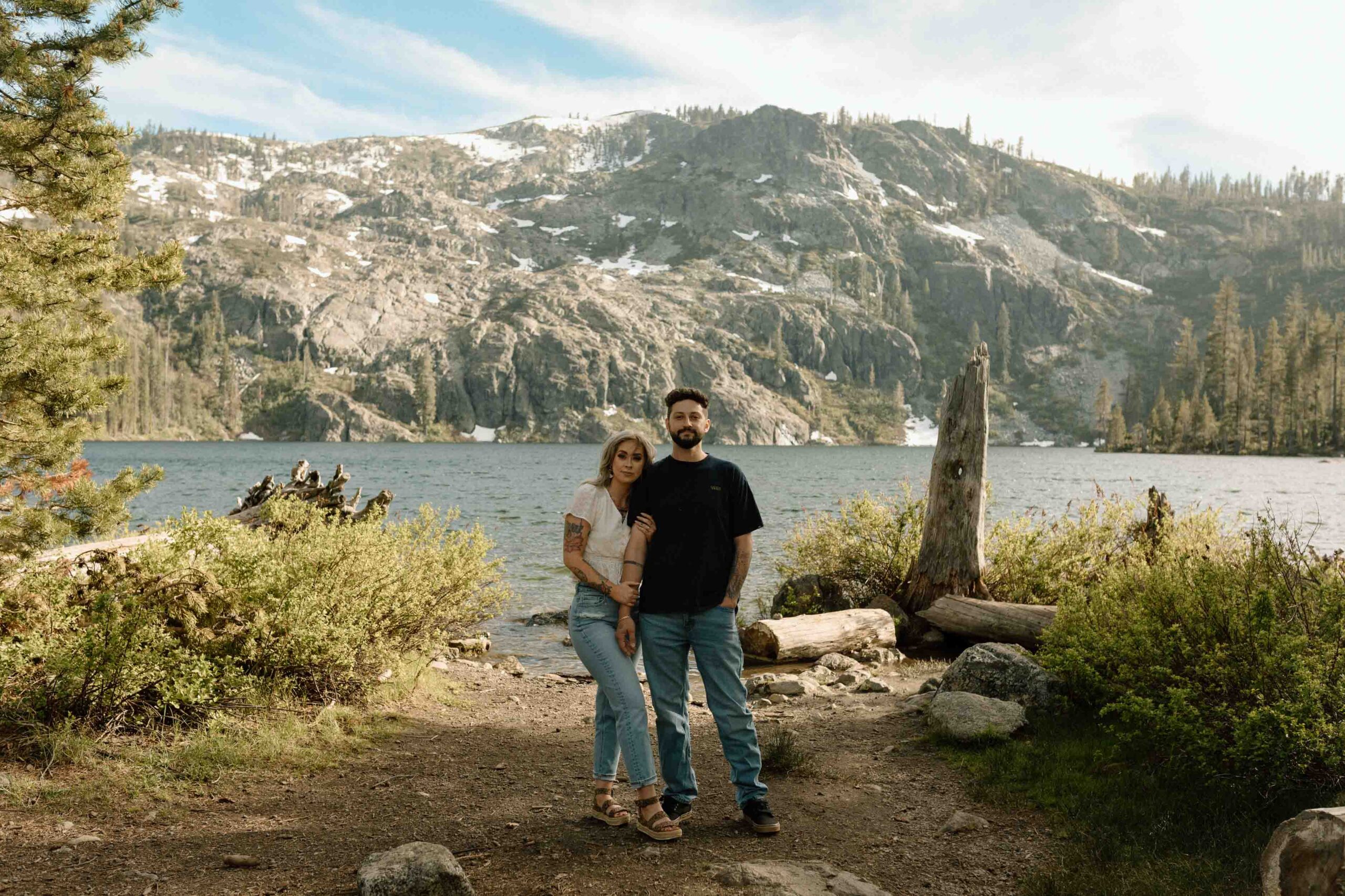 woman holding onto man's arm as they look into camera while surrounded by mountains and lake in California