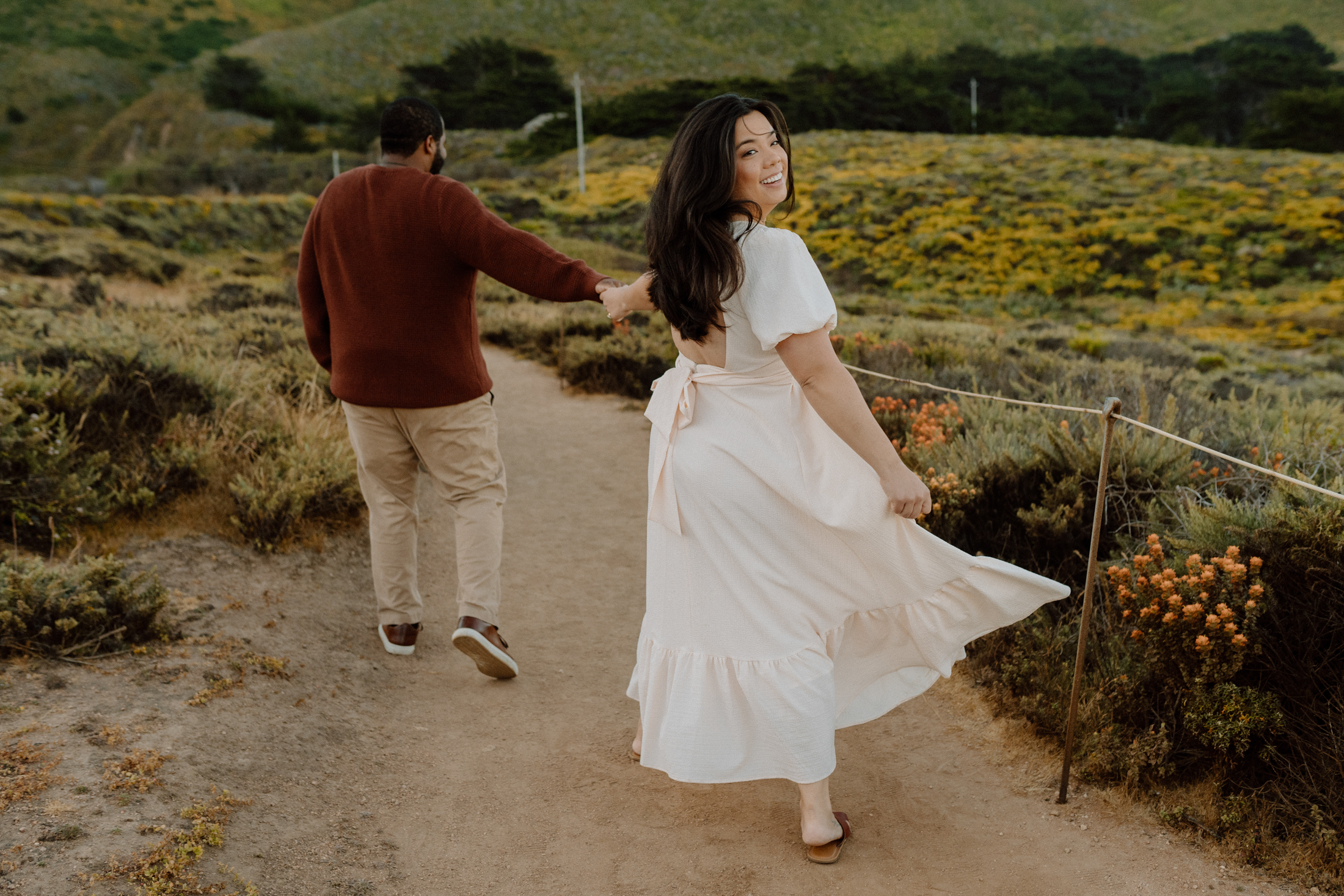 engaged couple walking away from camera, as girl looks back over her shoulder smiling