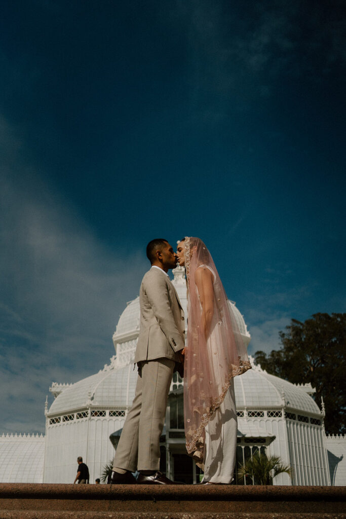 A newlywed couple kissing at the top of an outdoor staircase 
