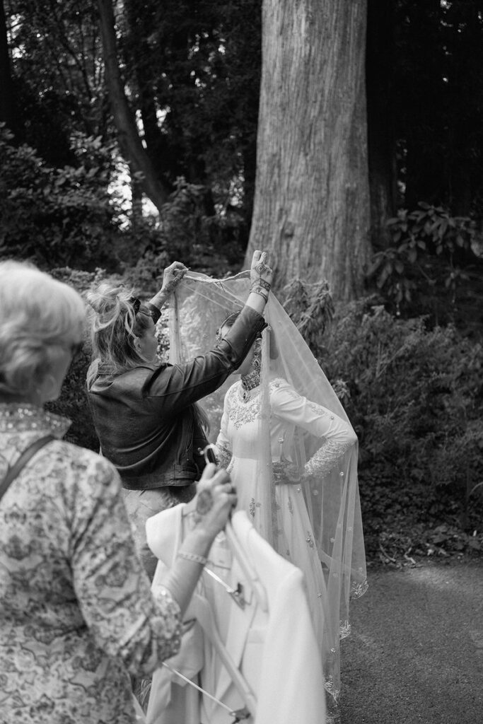 Wedding guests holding and adjusting a wedding outfit on a newlywed 