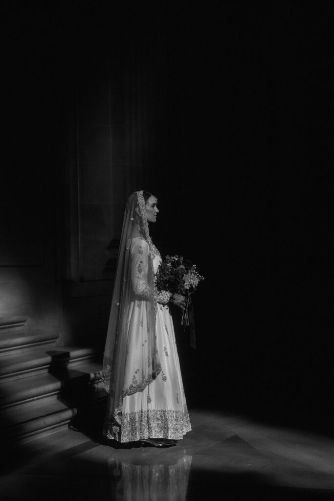 A person in a wedding dress standing at the bottom of a staircase holding a bouquet of flowers 