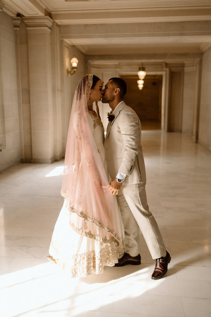 A newlywed couple kissing in an ornate hallway 