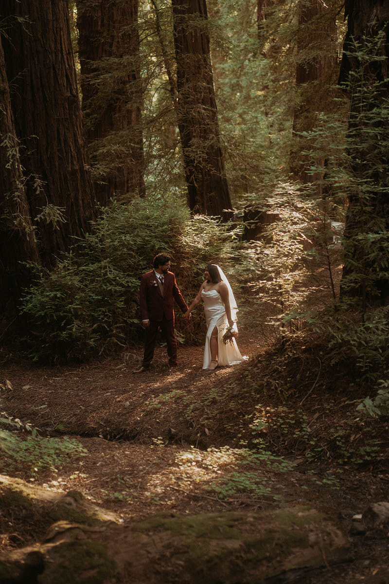 A newlywed couple holding hands and walking in the forest during their intimate elopement