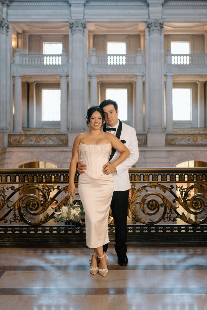 Newlyweds standing close together smiling in a grand hallway 