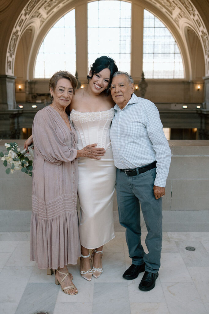 A newlywed smiling with their grandparents on either side of them 
