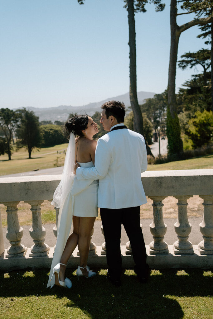 A newlywed couple standing on a lookout about to kiss 