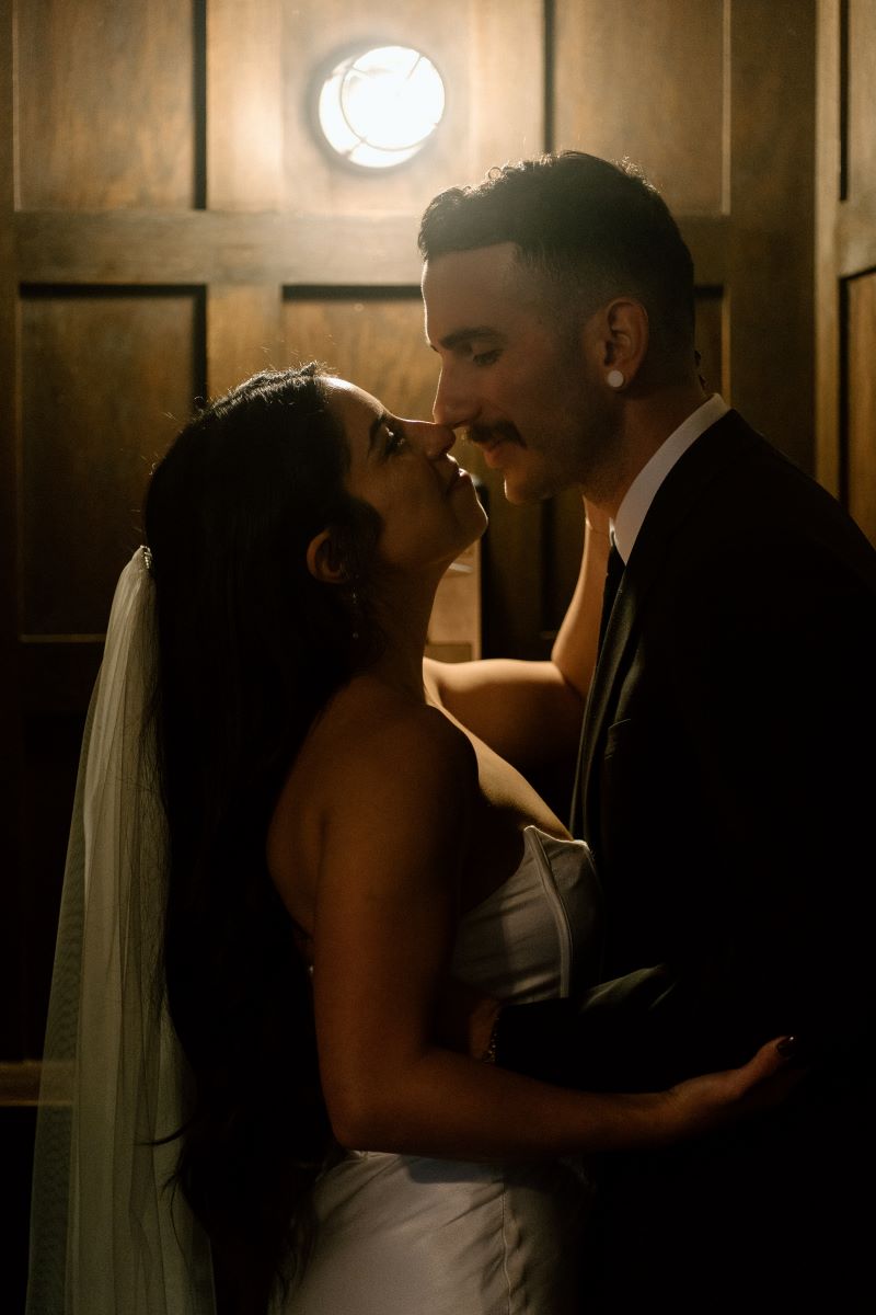 A couple inside of an elevator looking into each other's eyes and holding each other with their noses pressed together 