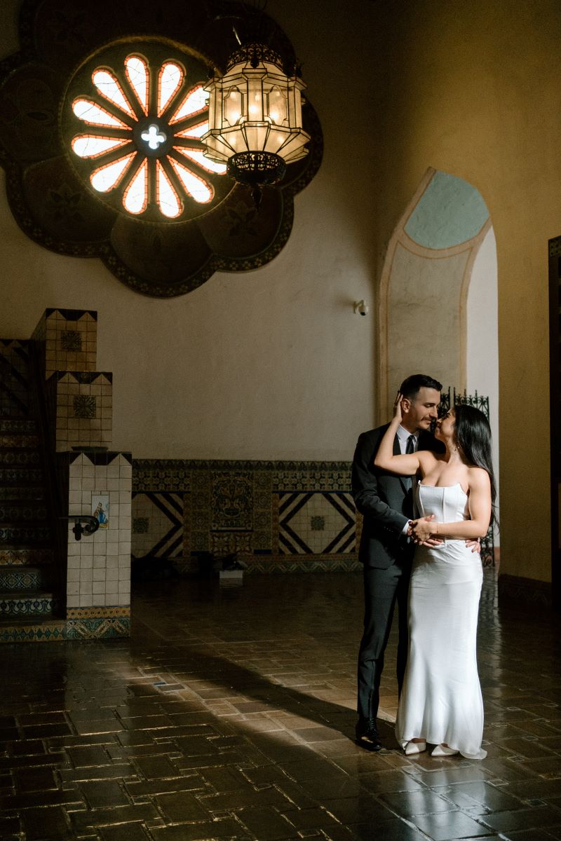 A couple inside of a courthouse they are both looking at each other and holding hands with her other free hand the woman is touching the side of her partner's face 